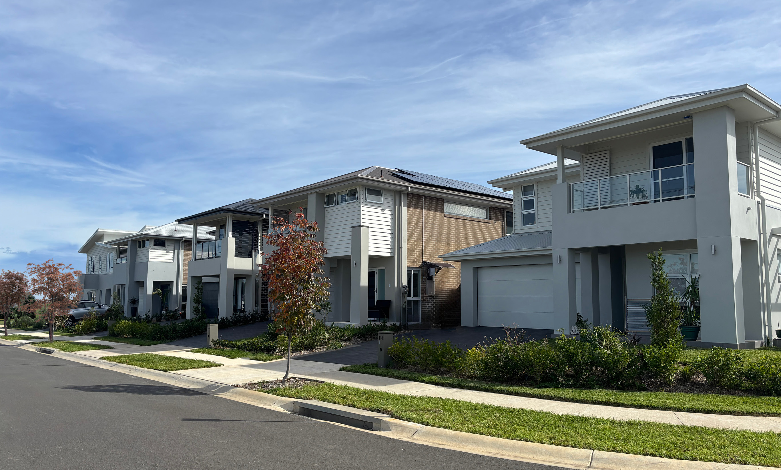 double-storey homes with balconys along a leafy street.