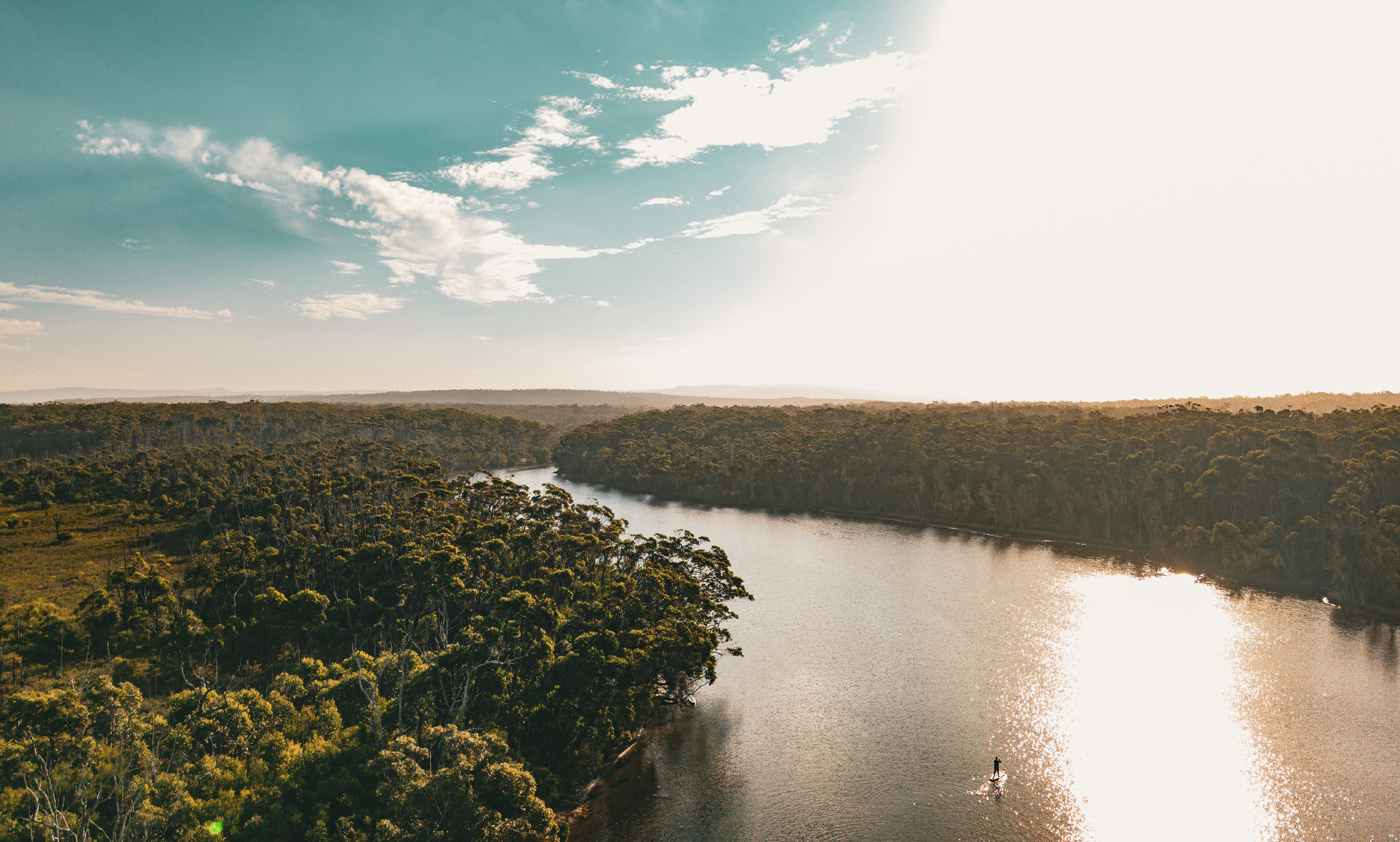 Paddleboarder on river that is surrounded by bushland at Jervis Bay region.