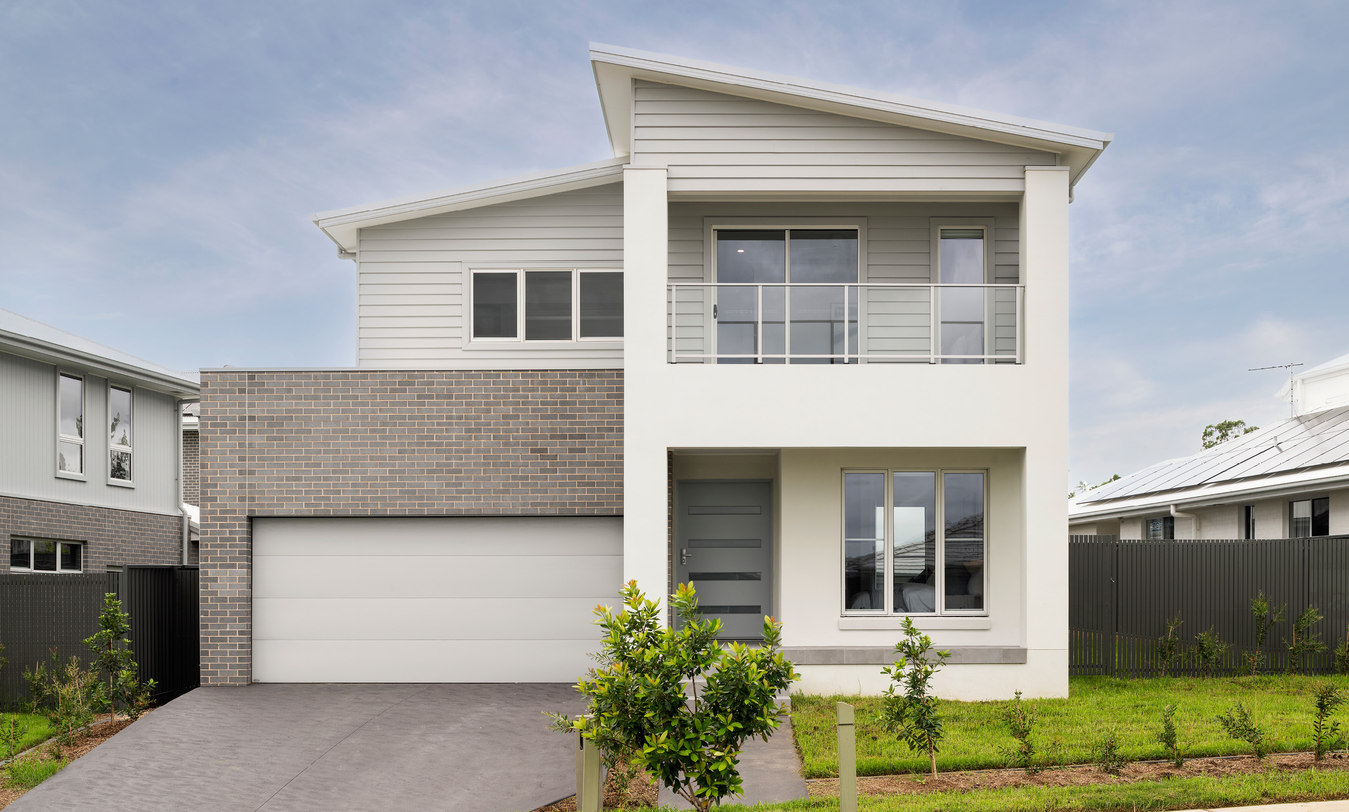 Double-storey home with brick and render features. Double garage on the left and a balcony on the right.