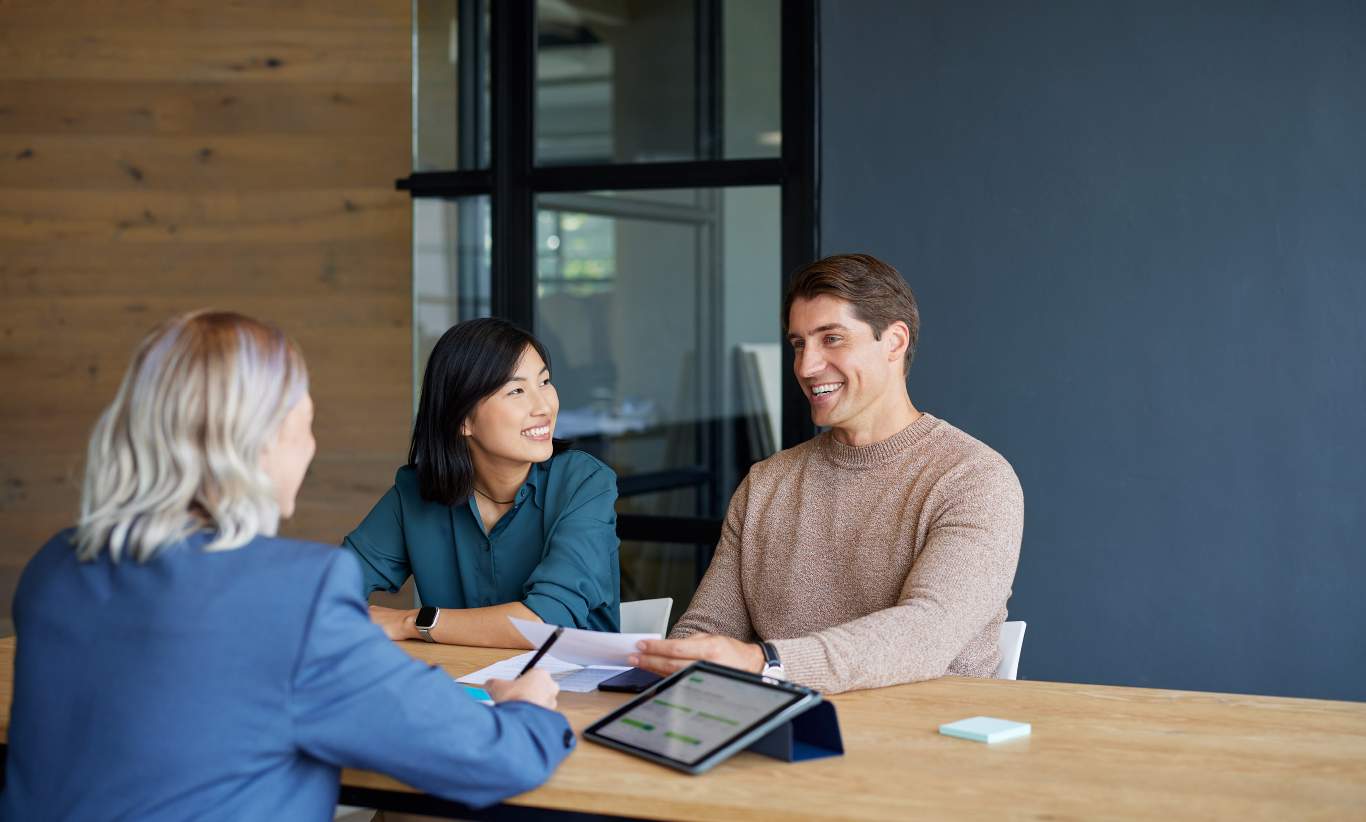 2 women and 1 man sitting around a board room table with iPad and paperwork on the table.
