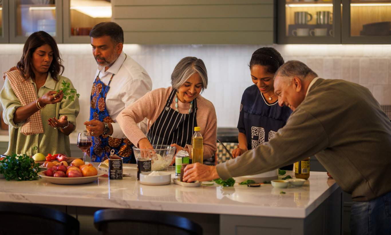 Multi-generational family gathered around the kitchen cooking dinner together.