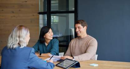 2 women and 1 man sitting around a board room table with iPad and paperwork on the table.