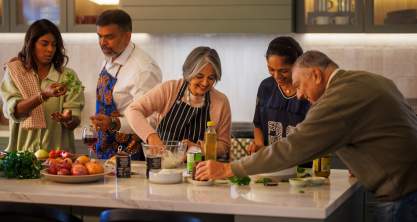 Multi-generational family gathered around the kitchen cooking dinner together.